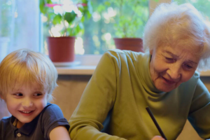 Elderly person writing while sitting next to a child