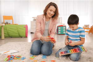 A woman and a young boy play together with colorful building blocks on a carpeted floor.