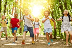 Group of children joyfully running on a sunny forest path.