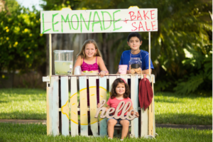 Children running a lemonade and bake sale at a homemade stand.